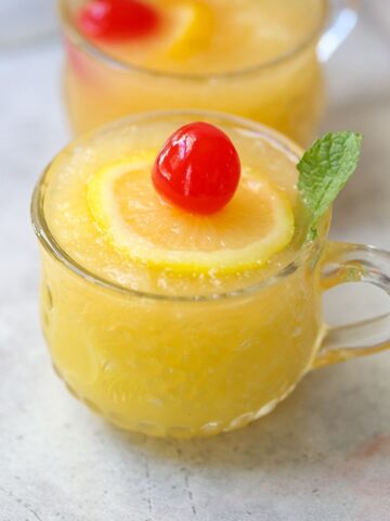 slushy pineapple party punch in small punch glass with lemon slice, mint leaf, and cherry on top