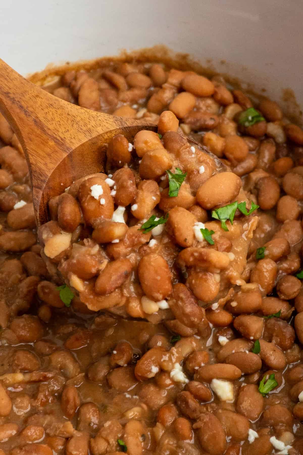 A wooden spoon scooping pinto beans from the slow cooker.