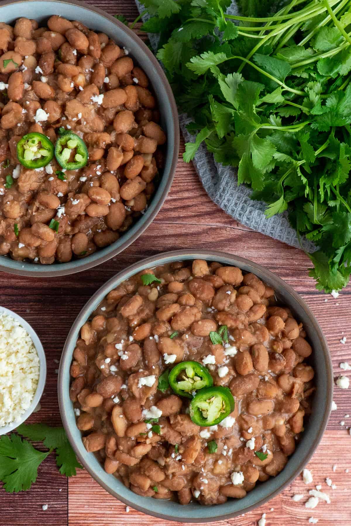 Two bowls of slow cooker pinto beans on a wood background.