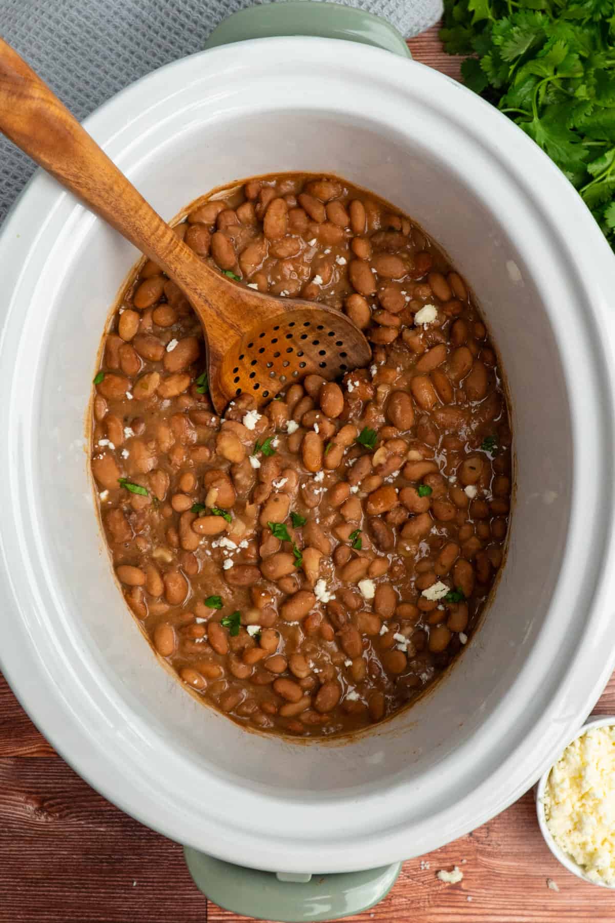 Overhead image of pinto beans in a crock pot with a wooden spoon leaning on the side.