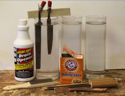 My equipment includes three glass flower vases I bought at Goodwill for 69 cents apiece. A thin stick and some small spring clamps hold the tangs out of the acid. Drain cleaner provides sulfuric acid to etch the files and a saturated baking-soda solution neutralizes the acid. The third vase has a fresh-water rinse. The file card (lower left) cleans file teeth and shop-made tools of copper, brass, and steel remove the debris the file card leaves behind.