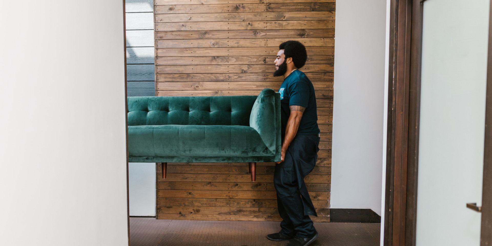 man moving an emerald green couch into an apartment home