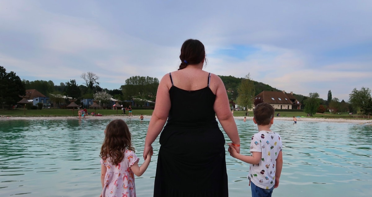 Woman hand in hand with boy and girl, looking out over a lake