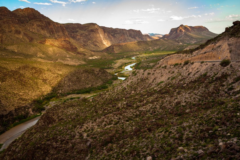 a desert mountain landscape covered in some foliage with a river winding through it at sunset