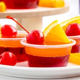 a bunch of containers of Tequila Sunrise Jello Shots topped with cherry and a slice of orange on a plate