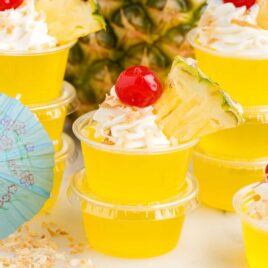 a close up shot of Pina Colada Jello Shots with one topped with a cherry and a slice of pineapple