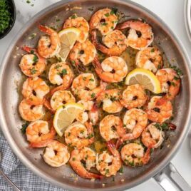 a skillet of shrimp and lemon slices garnished with parsley