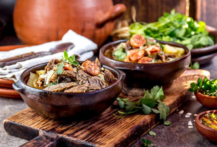 Rustic wooden table with two bowls of hearty stew, garnished with herbs, accompanied by fresh greens.