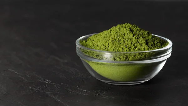 Chlorella green powder in a bowl on a stone black background. Spirulina powder or barley powder. Superfood. Space for text.