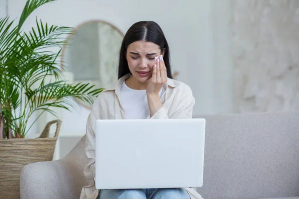 Quarantine. War. A beautiful young woman sits at home on the couch with a laptop, talks online via video link with her family and friends, cries, misses them. Wipes tears with a napkin.