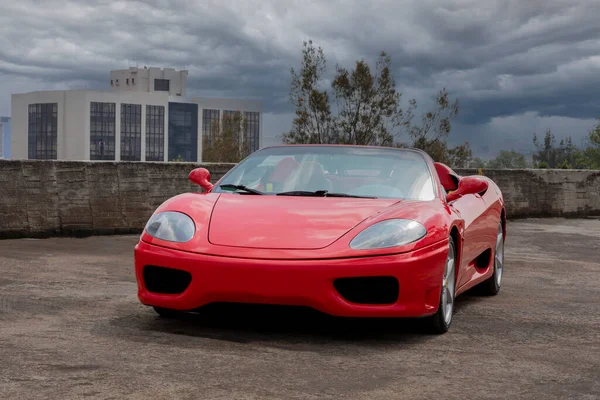 Red sports car on a city rooftop with buildings and cloudy sky in the background.