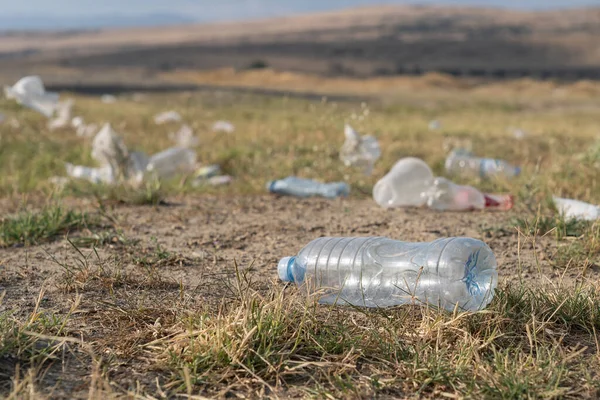 Rubbish from garbage dump spread by wind in rural area on summer day. Scattered plastic bottles and bags lie on grass in countryside causing pollution of environment. Ecological problem closeup view