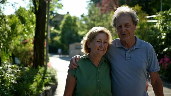 Two happy older people walking outside smiling, senior couple together in outdoor nature walk