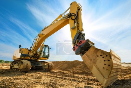 Foto de Gran excavadora en obra nueva, en el fondo el cielo azul y el sol - Imagen libre de derechos