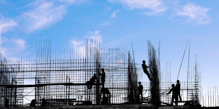 Foto de Los trabajadores en las siluetas del edificio en contra del cielo azul. Industria de la construcción y construcción bajo tema de construcción - Imagen libre de derechos