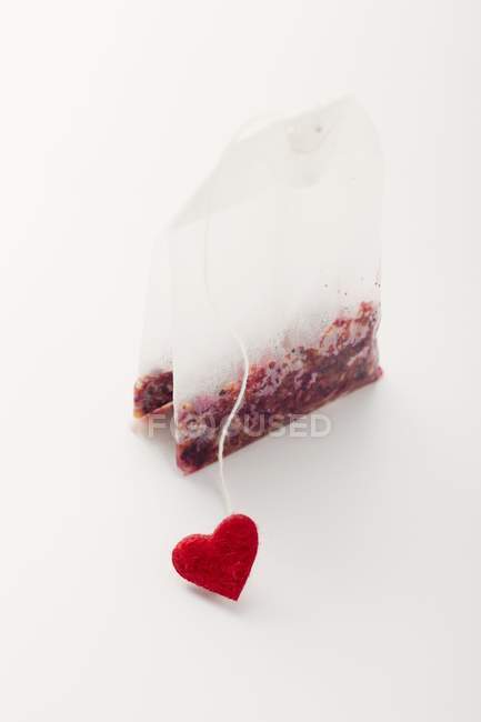 Closeup view of one tea bag with red heart on white surface — Stock Photo