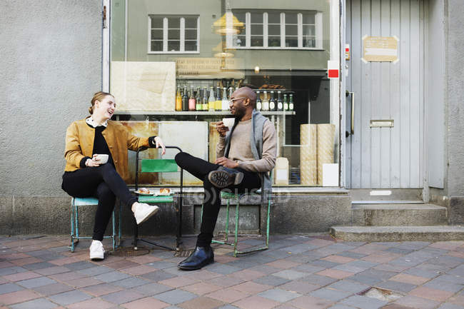 Friends holding cups while sitting on chairs — Stock Photo