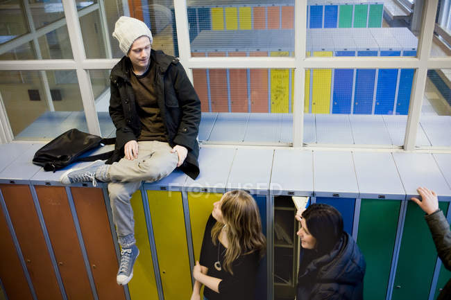 High angle view of man sitting on lockers while looking at female friends in university — Stock Photo