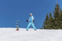 Little boy in winter clothing learning skiing with father at snowy resort. — Stock Photo