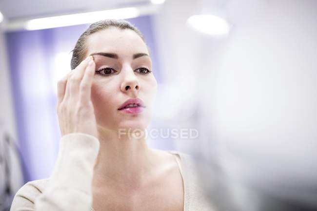 Woman looking at face in mirror in cosmetic clinic. — Stock Photo