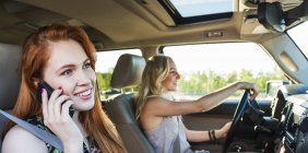 Two girls sitting in car while one driving another one speaking on cell phone — Stock Photo