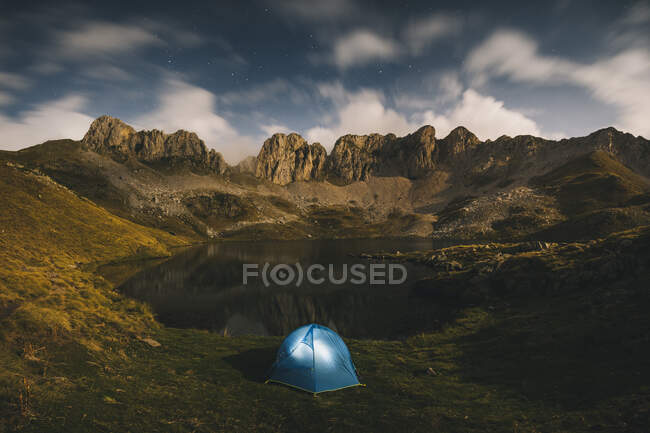 Lighted tent against rugged mountains and lake, Pyrenees. — Stock Photo