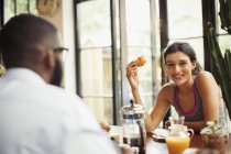 Portrait smiling young woman enjoying croissant and coffee in cafe — Stock Photo