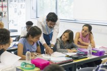 Male teacher helping junior high school students at desk in classroom — Stock Photo