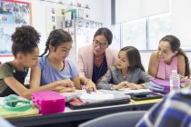 Female teacher and junior high school students studying at desk in classroom — Stock Photo