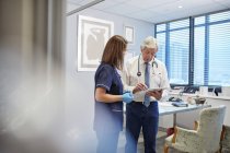 Doctor and nurse with digital tablet talking, consulting in clinic doctors office — Stock Photo