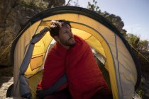 Hiker wrapped in blanket sitting in tent on a sunny day — Stock Photo