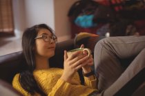 Thoughtful woman lying and having coffee on sofa at home — Stock Photo