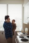 Father talking on mobile phone while holding baby in kitchen — Stock Photo