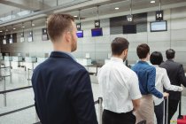 Passengers waiting in queue at a check-in counter with luggage inside the airport terminal — Stock Photo