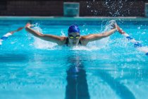 Front view of young female swimmer with swim goggle swimming at swimming pool — Stock Photo