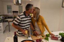 Front view of mature Caucasian couple kissing each other while preparing pizza in kitchen at home — Stock Photo