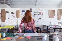 Rear view of a young Caucasian female fashion student looking at drawings on the wall while working on a design looking at designs on a wall in a studio at fashion college — Stock Photo