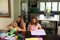 Front view of a young Caucasian woman doing crafts with her tween and younger daughters in their sitting room — Stock Photo