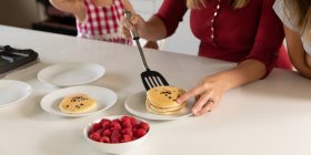 Front view close up of woman making pancakes in the kitchen at home with her tween and younger daughters — Stock Photo