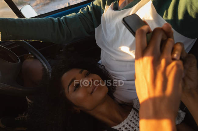 High angle view of young African American man driving while pretty mixed race woman using mobile phone in car — Stock Photo