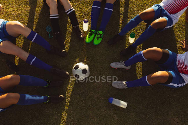 High angle view of female soccer players sitting in a circle with ball in between — Stock Photo