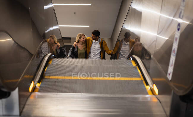 Front high angle view of a Caucasian couple out and about in the city, going up in underground station with an escalator, smiling and embracing. — Stock Photo