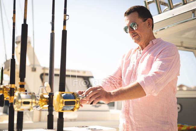 Un uomo caucasico, indossando una camicia rosa e occhiali da sole scuri godendo il suo tempo su una barca, tenendo una canna da pesca — Foto stock