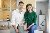 Couple sitting on kitchen counter and smiling — Stock Photo