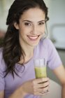 Woman holding glass of vegetable smoothie and smiling — Stock Photo