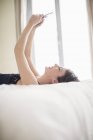 Laughing woman lying on bed and using a mobile phone — Stock Photo