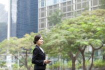 Chinese businesswoman looking with digital tablet in hands on street — Stock Photo