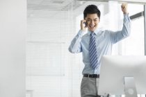 Cheerful Chinese businessman talking on phone in office — Stock Photo