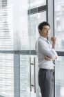 Chinese businessman standing by window and looking in camera — Stock Photo