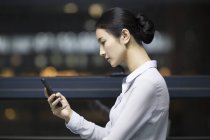 Side view of Chinese businesswoman using smartphone in office building — Stock Photo